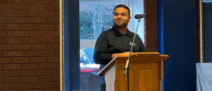 Ishaan stands a the podium in the dining hall smiling out to students